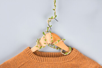 Orange sweater on hangers entwined with plants on gray background with copyspace. Conscious and environmentally friendly consupmtion - new modern trends in shopping. Zero waste. Slow fashion concept.