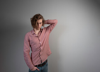 Young handsome man in coral shirt posing against grey wall background .