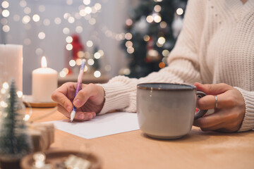 Goals plans make to do and wish list for new year christmas concept writing in notebook. Woman hand holding pen on notepad and coffee cup at home on winter holidays xmas. - obrazy, fototapety, plakaty