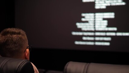 Side view of a young man watching the credits after watching a movie in a cinema.