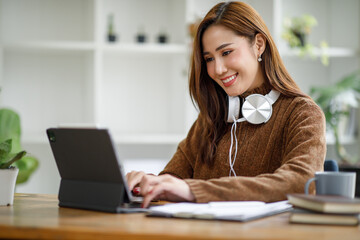 Young attractive university student using a laptop computer, studying online at home. Cheerful caucasian Asian woman writes notes, planning working process, sitting at home. Exam preparation. 