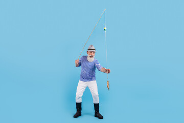 Full body photo of happy positive old man catch fish rod smile good mood isolated on blue color background