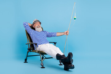 Full body photo of positive relaxed old man sit chair vacation fisherman isolated on blue color background