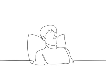 man sits in bed under his back pillow - one line drawing vector. concept of being at home reclining in bed