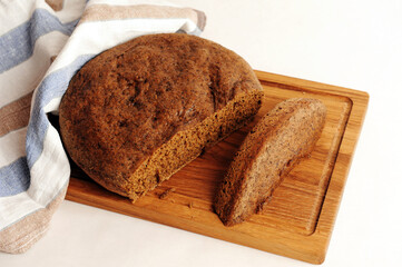Fresh homemade round malted rye bread on wooden board. White background, linen fabric