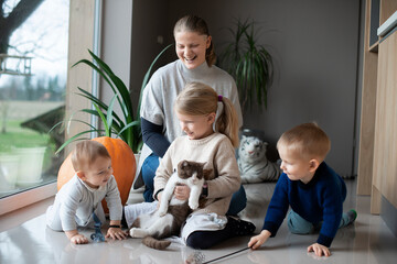 mother with her three children playing with a cat on the floor at home