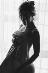Black and white portrait of blond young beautiful woman having fun hiding under white sheet...