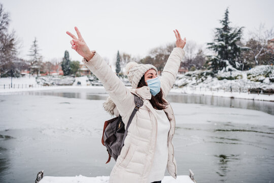 happy backpacker woman wearing face mask standing on pier in front of frozen lake in city. travel and Lifestyle during winter in city during pandemic corona virus