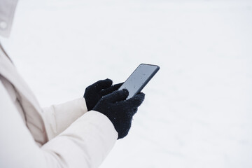 unrecognizable woman walking outdoors in city during winter while snowing, using mobile phone.winter lifestyle