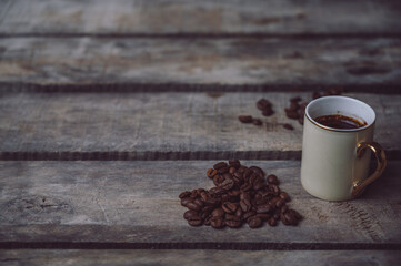 Hot coffee in mini white coffee cup and coffee beans in a heart shape on a rustic wooden background with copy space