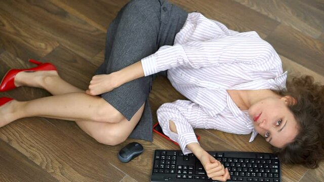 Tired young female office manager is lying on the floor with keyboard, mouse and smartphone, lay flat movement, routine work, freelance, burnout syndrome