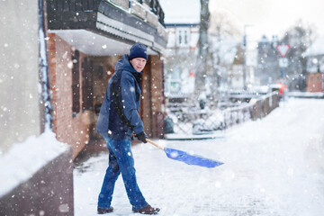 Man with snow shovel cleans sidewalks in winter during snowfall. Winter time in Europe. Young man...