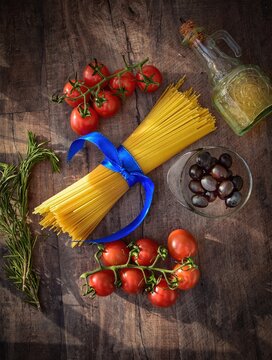 Moscow, russia, july 2021, spaghetti tied with a blue ribbon, tomatoes on a branch, rosemary, olives and olive oil in a bottle lie on a wooden background