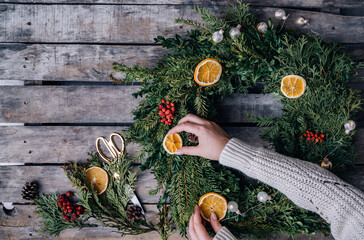 Top view of florist hands making Christmas wreath on wooden tabletop