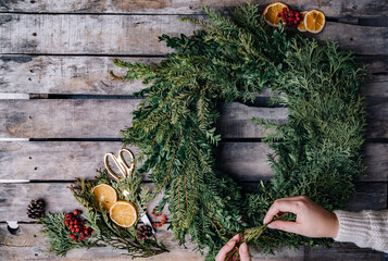 Top view of florist hands making Christmas wreath on wooden tabletop
