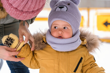 Mom puts a mitten on a baby in a yellow jacket in winter