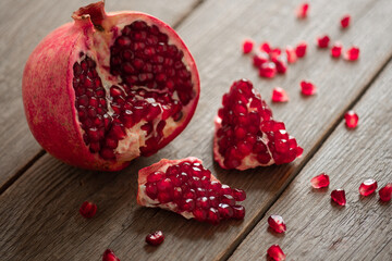 ripe open pomegranate on a wooden table red grains are scattered around