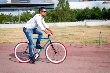 A handsome casual man is going to the office by bicycle. He is driving bike in front of office district.