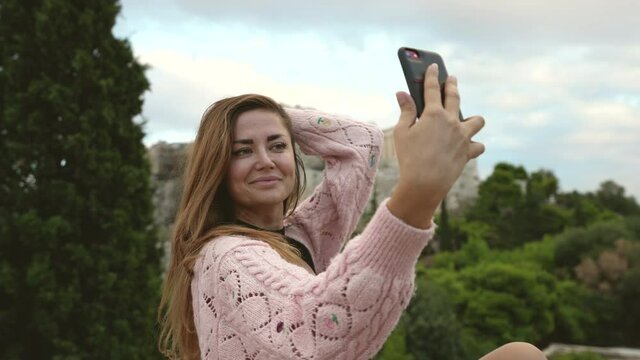 Young adult female traveling tourist with phone takes selfie with Acropolis hill, ruins of Athens. Traveler in vacation trip photographs Greece, shoots iphone pictures of herself. Temples tourism.