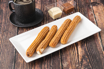 Hot churros with chocolate sauce on wooden table