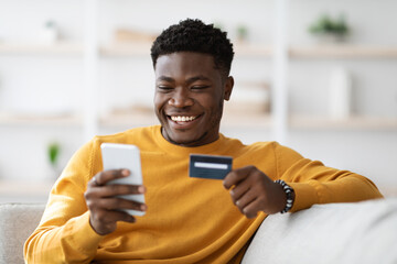 Positive black man using cellphone and credit card at home