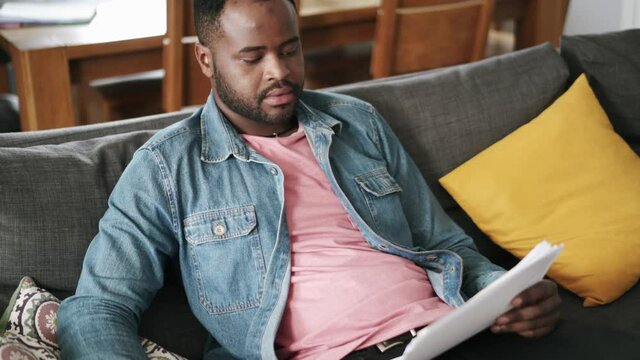 African man reading papers at home on the sofa