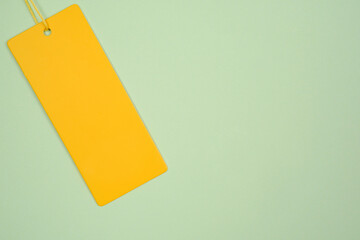 An empty price tag, a gift tag or a yellow label with a yellow cord on a delicate green background.