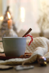 Cup of warm drink with candy cane and cinnamon stick, soft blanket and various Christmas decorations. Hygge at home. Selective focus.