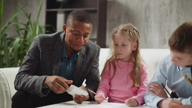 Black English teacher shows cards and tells letter names to little children studying foreign language during lesson with native speaker slow motion