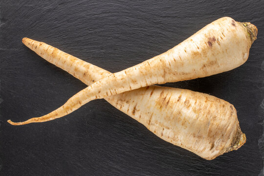 Two fragrant parsnip roots on a slate stone, close-up, top view.