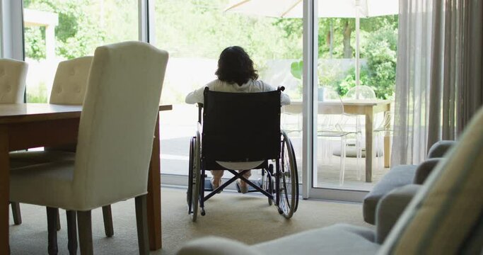 Biracial disabled woman in wheelchair drinking coffee and looking out of window in sunny living room