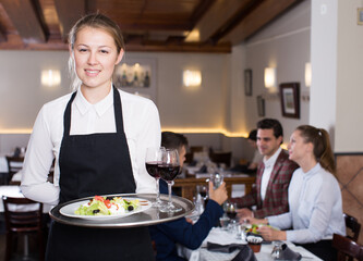 Fototapeta na wymiar Attractive young waitress with serving tray welcoming to restaurant