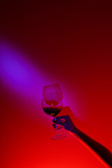 Fototapeta na wymiar Closeup of anonymous woman hand holding glass of wine over fashion blue wall, neon blue stripe on wall. Colorful light, minimalism concept. 