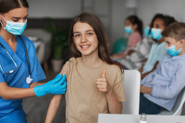 Happy Vaccinated Girl Gesturing Thumbs Up Approving Antiviral Vaccine Indoor