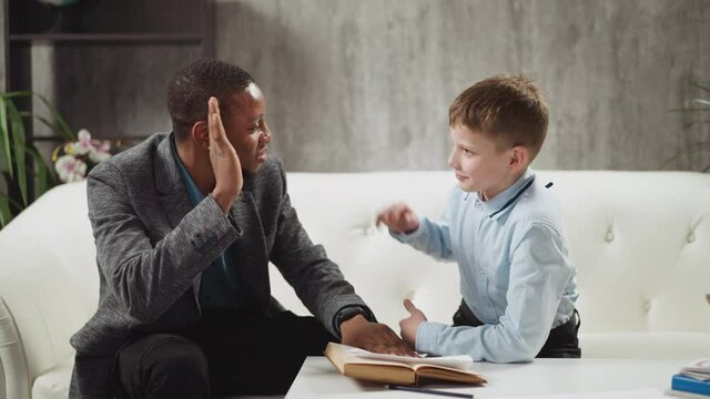 Cheerful African-American tutor gives high five and shows thumb-up praising junior boy student at private English tuition with native speaker slow motion