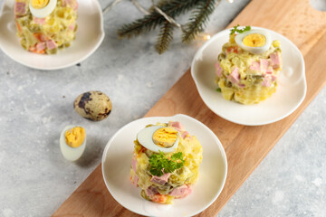 Buffet portions of olivier salad decorated with quail eggs. Close-up, fir branches and a garland in the background. Selective focus