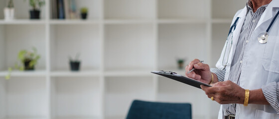Cropped shot of doctor in uniform with stethoscope taking notes in medical history of patient on clipboard