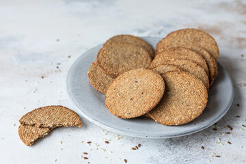 Plate with tasty crackers with sesame and flax seeds on grey stone background.