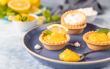 Lemon curd mini tarts decorated with mint and lemon slices on blue ceramic plate.