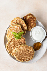 Tasty oatmeal pancakes served with jam and natural yogurt on ceramic plate, light concrete background.