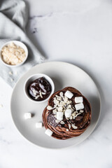 Chocolate pancakes with melted chocolate, ground almond and marshmallow, light background.