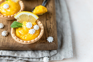 Lemon tartlets. Homemade shortbread mini tarts with lemon curd and meringue on wooden board, light...