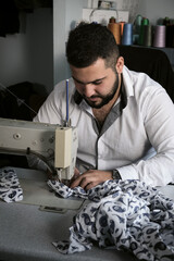 Middle eastern male tailor in white shirt working on sewing machine , while makes alterations at...