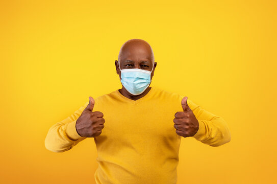 Senior Black Man Wearing Face Mask, Gesturing Thumb Up, Approving Coronavirus Protection On Orange Background