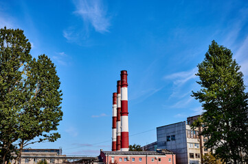 Three smoke pipe made of bricks standing tall with blue sky and trees behind it during a summer day