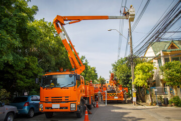 An orange crane lift sending workman with safety on a bucket to repair a light pole in the village