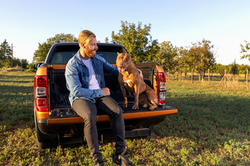Best friends sitting in the back of a pickup truck, young bearded man and his American bully canine companion © didesign