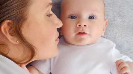 Happy newborn baby with his mother. Healthy newborn baby in a white t-shirt with mom. Closeup Faces of the mother and infant baby. Cute Infant boy and parent, top view. Happy family portrait
