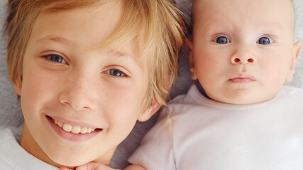 Smiling faces of the brothers, top view. Happy newborn baby with his brother. Healthy newborn baby in a white t-shirt with brother. Closeup Faces of the brothers. Happy family