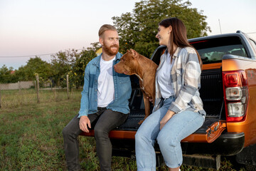 Two young people and a bully dog sitting on the cargo bed door of a pickup truck looking for...